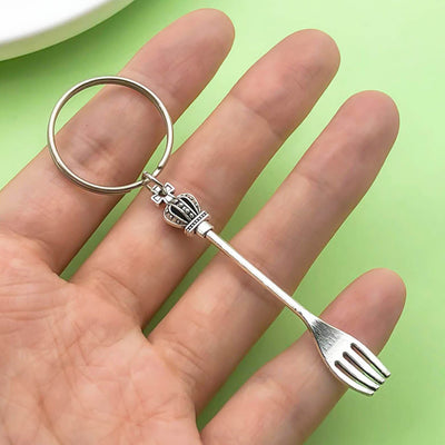 A hand holds a silver-tone crown fork keychain over a green background.