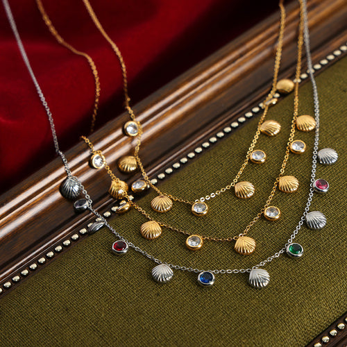 Gold and steel shell charm necklaces with clear and colored stones on green fabric