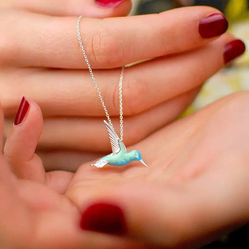 Blue green enamel hummingbird pendant necklace held in hands with red nails