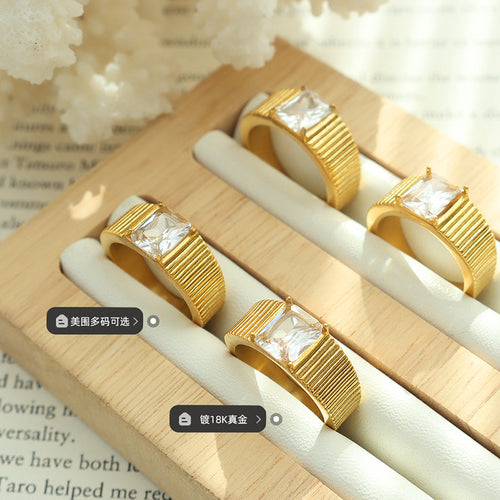 Four gold ribbed square-stone rings on wooden display with labels