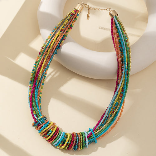 Multicolor beaded multi-strand necklace draped over a white ceramic stand with a gold-tone clasp