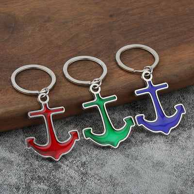 Three anchor keychains in red, green, and blue on a wood and gray surface.