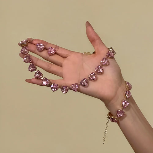 Pink gold heart crystal necklace bracelet and studs held across open hand