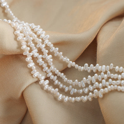 Coiled strands of white oval faux pearl beads on champagne satin fabric