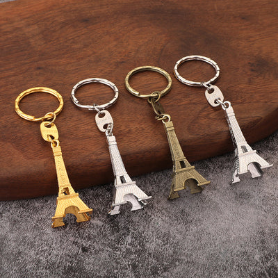 Four Eiffel Tower keychains in gold, silver, and antique bronze tones displayed on wood.