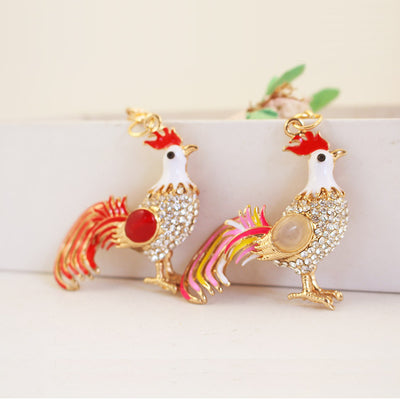 Two gold-tone rhinestone rooster charms with red and pale oval accents.