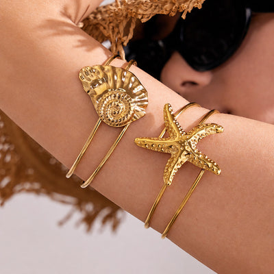 On-wrist view of sea shell and starfish open cuffs in main image 1.