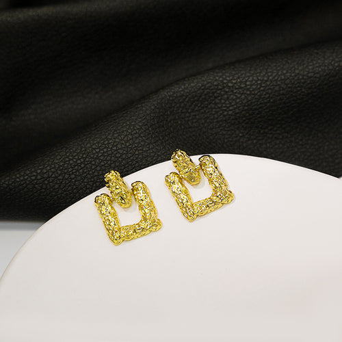 Gold textured open square studs on white round surface with black leather