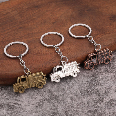 Three fire engine keychains in bronze, silver, and copper tones on a wood and gray surface.