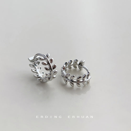 Silver olive leaf huggie hoops lying open on pale surface