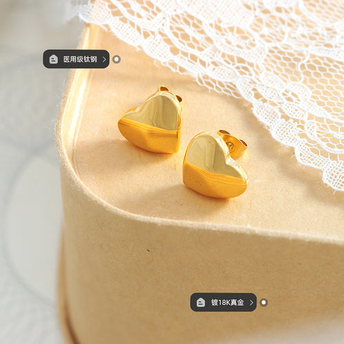 Pair of gold heart studs on tray with titanium and plating labels