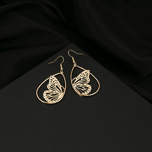 Gold butterfly teardrop earrings on black fabric surface