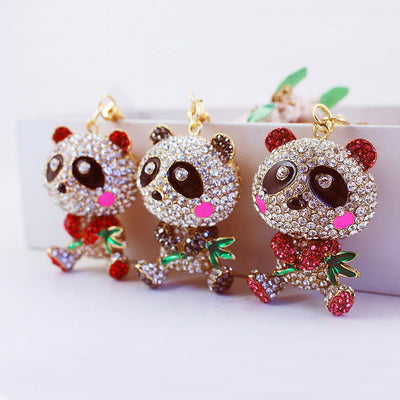 Three rhinestone panda keychains with pink, red, and black accents beside a white planter.