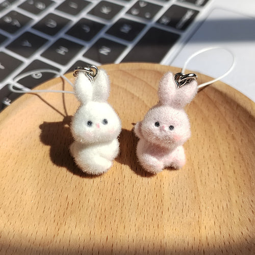 White and pink flocked bunny charms with white cords on wooden plate