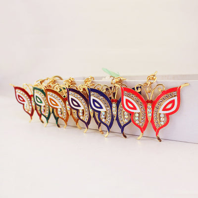 Six colorful butterfly keychains arranged in a row against a white block.