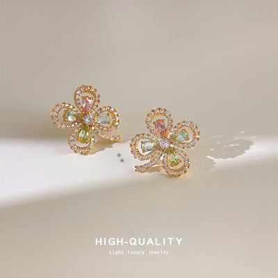 Gold four-leaf clover pastel crystal stud pair on cream surface