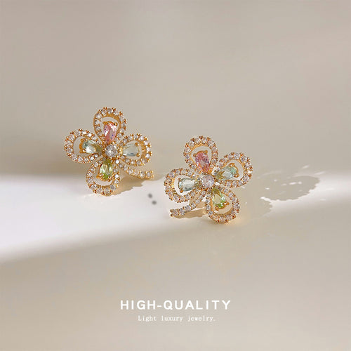 Gold four-leaf clover pastel crystal stud pair on cream surface
