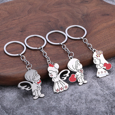 Four silver-tone keychains display winged and red-heart couple designs on a wooden surface.