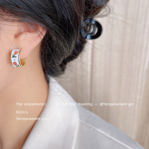 Model wearing gold white enamel tulip open hoop stud