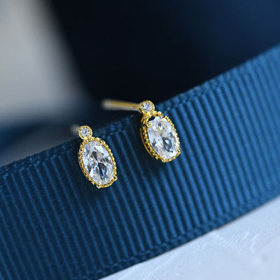 Gold clear oval mini studs on dark blue ribbon close-up