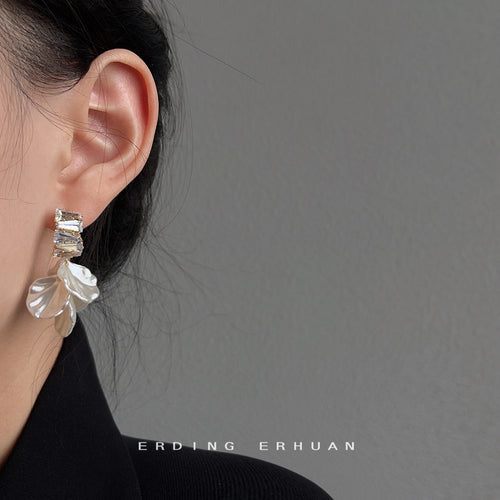 Gold-tone clear-stone-bar translucent-white-petal studs shown worn on an ear.