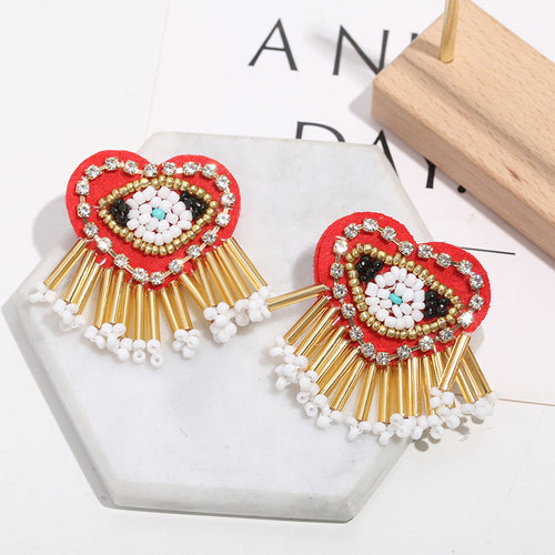 Red heart beaded earrings with gold fringe on a marble tile beside a wood block
