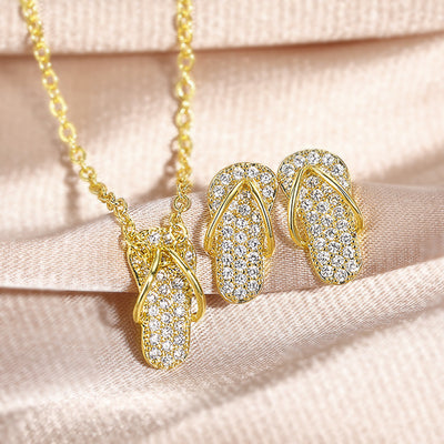Gold flip-flop CZ necklace and matching stud earrings on beige fabric