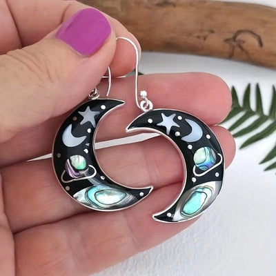 Crescent moon abalone earrings held in hand with purple nails