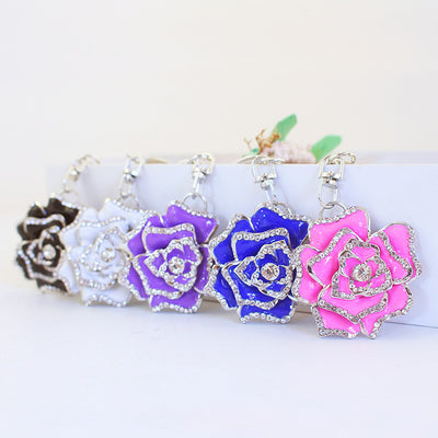 Five rose keychains in black, white, purple, blue, and pink are arranged in a row.