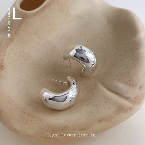 Silver polished C hoop studs on beige ceramic dish