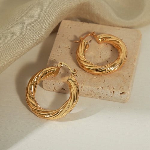 Gold twisted hollow hoops on stone block and fabric