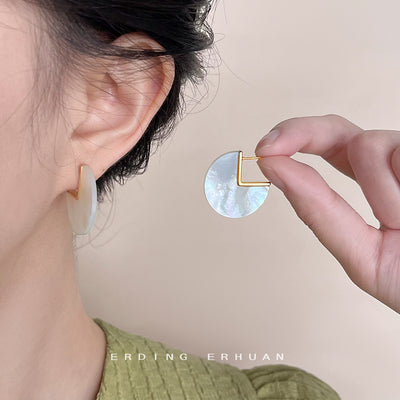 White pearlescent disc stud earrings with square cutout held beside an ear.
