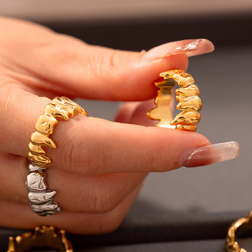 Hand holding gold flame-spike band ring with steel ring on finger