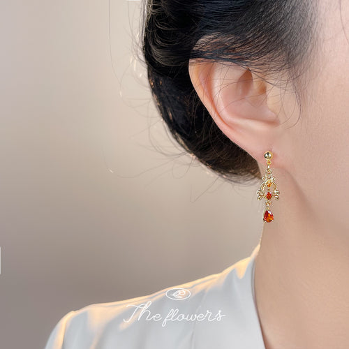 Model wearing gold filigree earring with amber teardrop on right ear