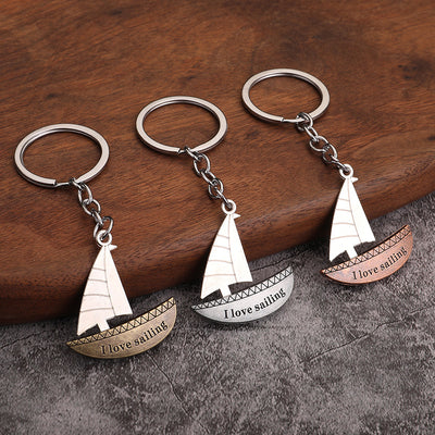 Three sailboat keychains in bronze, silver, and copper tones on a wooden surface.