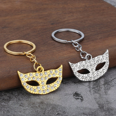 Gold-tone and silver-tone mask keychains displayed together on a wooden surface.