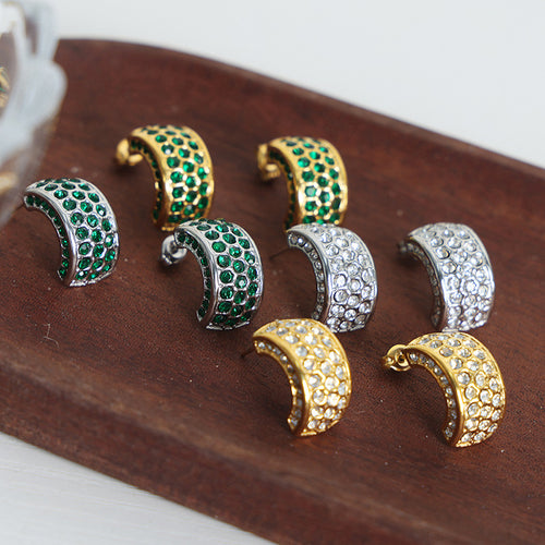 Mixed gold and steel C-shape pave crystal hoops on dark wood board