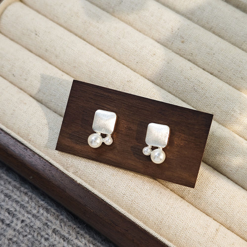 Silver brushed square dual pearl stud earrings on dark wood block