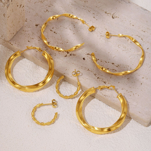 Gold twisted hoop earring styles arranged on stone slab