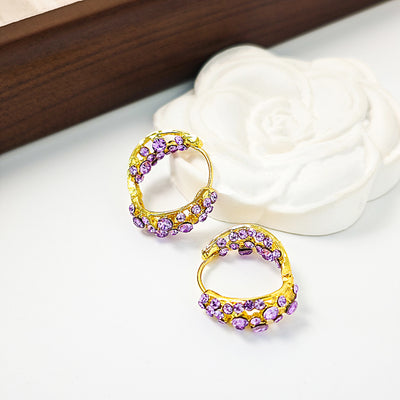 Gold purple rhinestone openwork huggies beside white rose and wood
