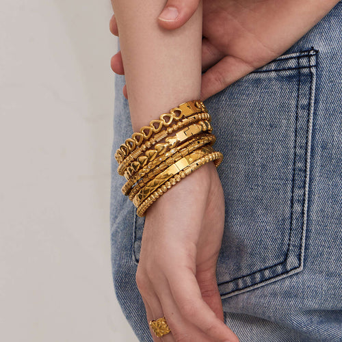 Stack of gold geometric heart and rope clasp bangles on wrist with jeans