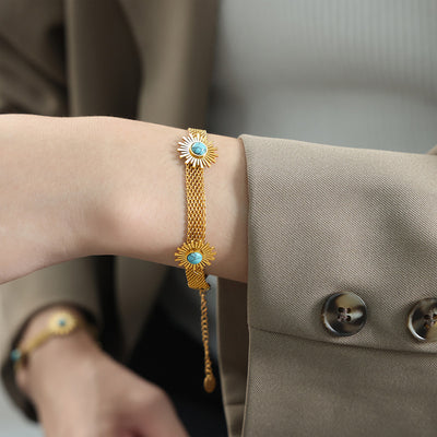 Model wrist wearing gold mesh bracelet with turquoise sunburst charms