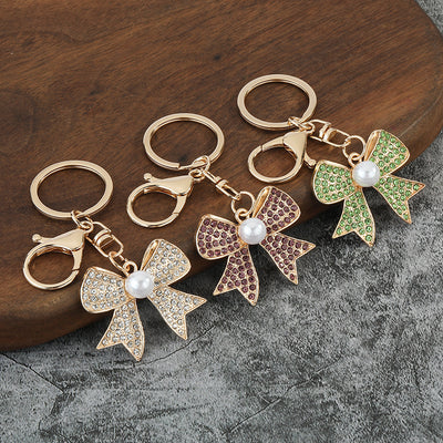 Three gold-tone bow keychains with white, purple, and green rhinestones.