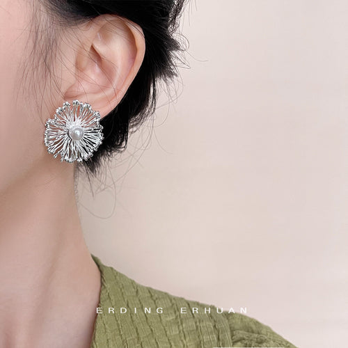 Silver-tone radiating wire flower and pearl studs shown worn on an ear.