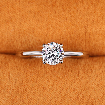 Silver four-prong clear round solitaire ring on orange fabric