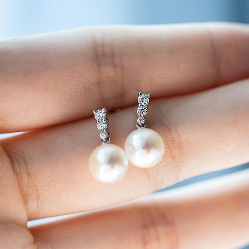 Pair of white pearl crystal bar earrings held on fingertips