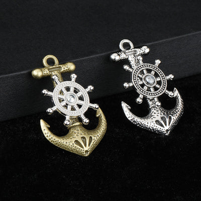 Antique bronze and silver-tone anchor charms with ship's wheel detail side by side on a black box edge
