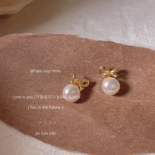 Gold-tone bow white-pearlescent drop studs shown worn on an ear.