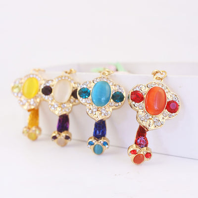 Four gold-tone ruyi-shaped pendants in yellow, purple, blue, and red are arranged on a white surface.