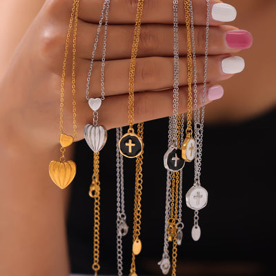 Hand holding gold and silver heart and cross pendant necklaces